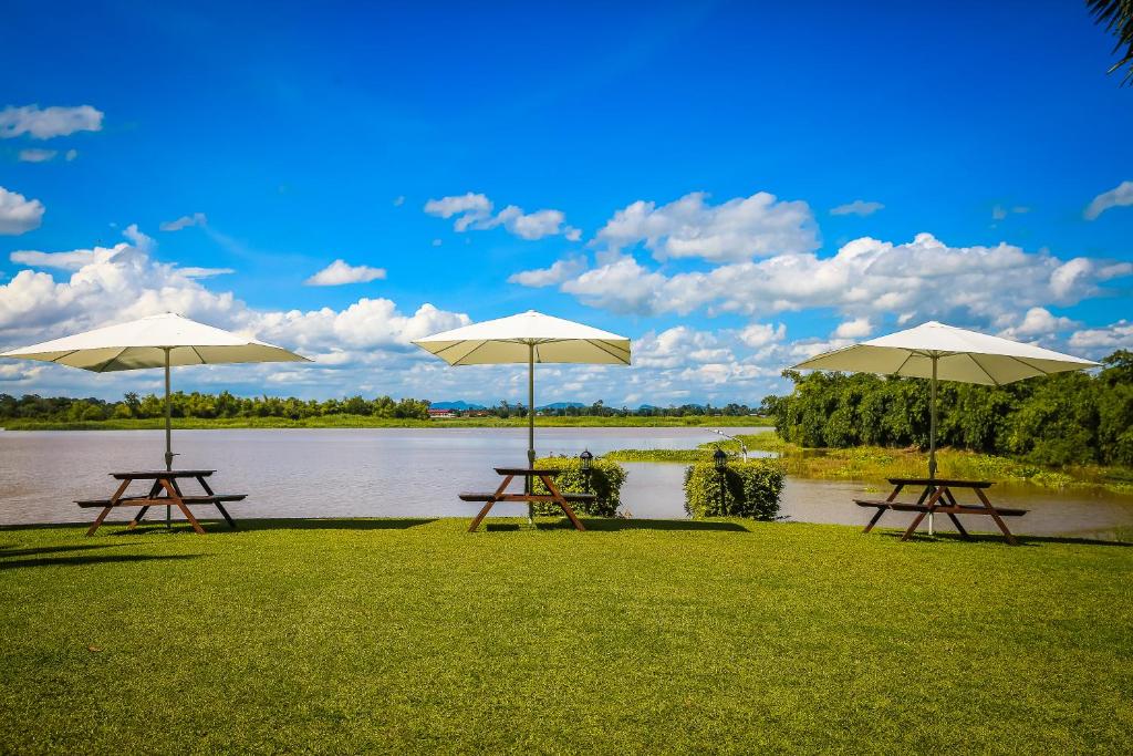 three picnic tables with umbrellas in front of a lake at Uthai River Lake Resort in Ban Nong Nam Khan