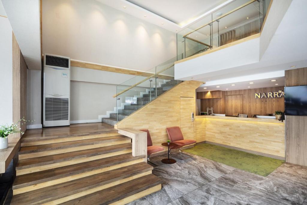 A compact lobby with a wood reception desk, staircase and glass-railed upper level.