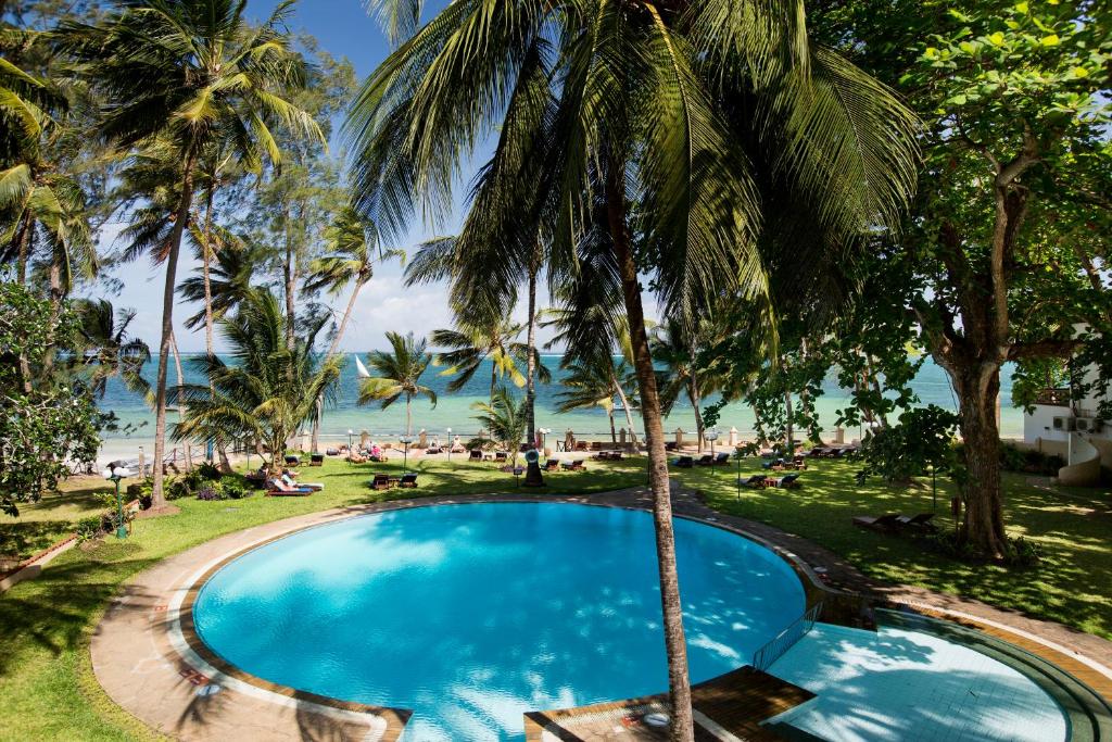 uma piscina com palmeiras e o oceano ao fundo em Neptune Beach Resort - All Inclusive em Bamburi