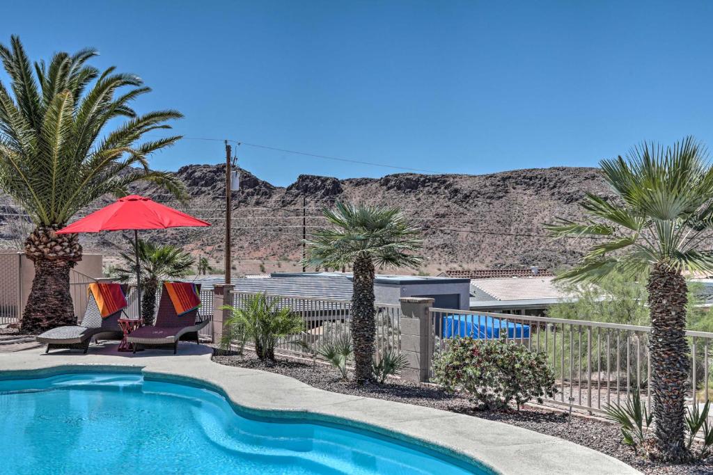 a swimming pool with palm trees and a red umbrella at Lake Havasu Home with Heated Pool, Spa and Mtn Views! in Lake Havasu City