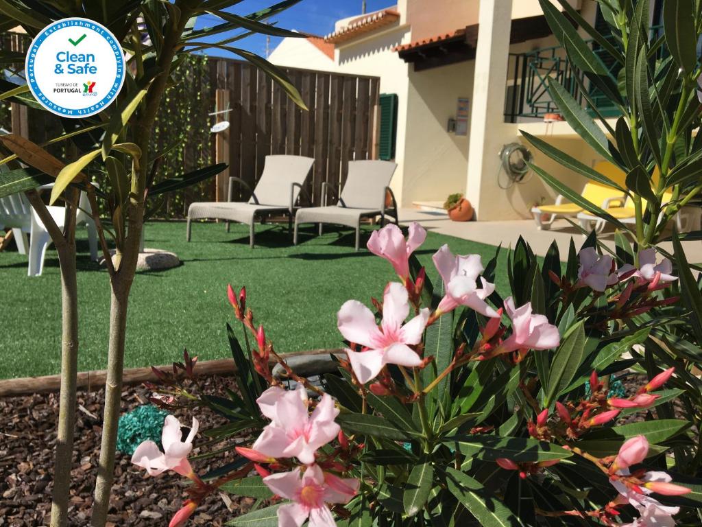 a garden with pink flowers and chairs in a yard at Casa Maré in Sagres