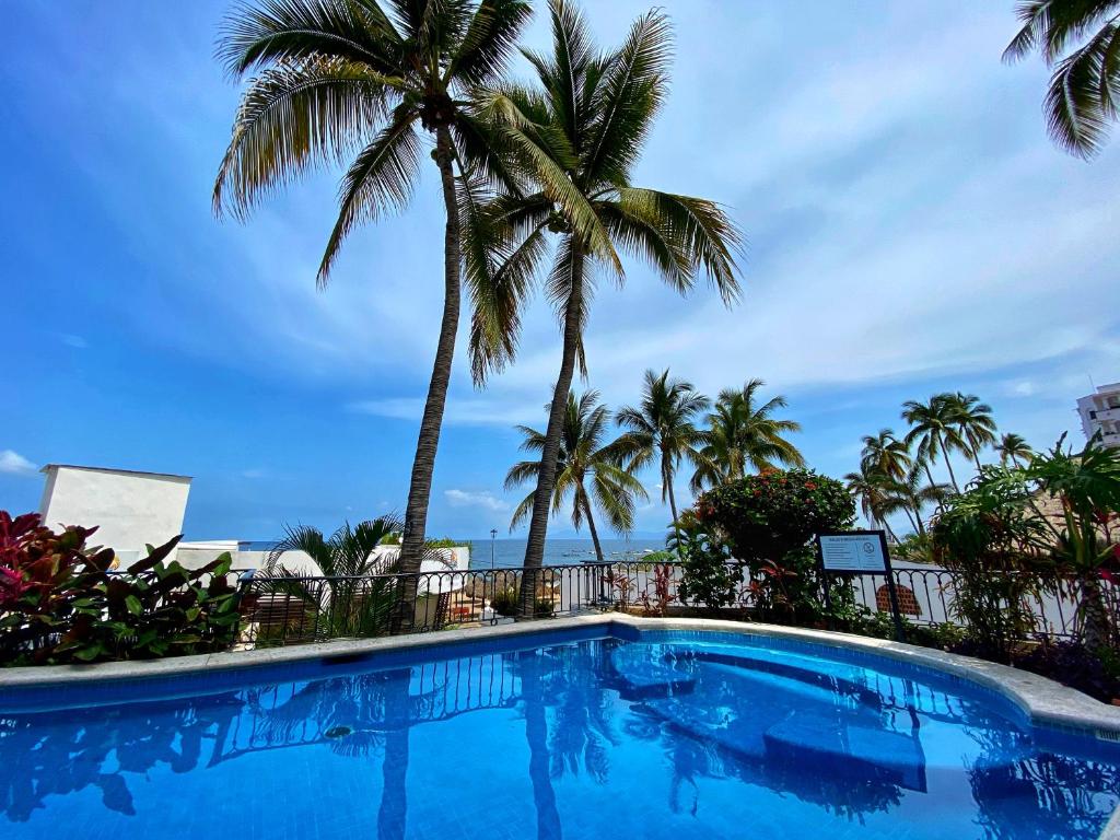 una piscina con palmeras y el océano en One Beach Street Zona Romantica Puerto Vallarta en Puerto Vallarta