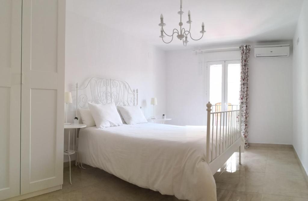 a white bedroom with a white bed and a chandelier at Muro de los Navarros 26-Apartamentos in Seville