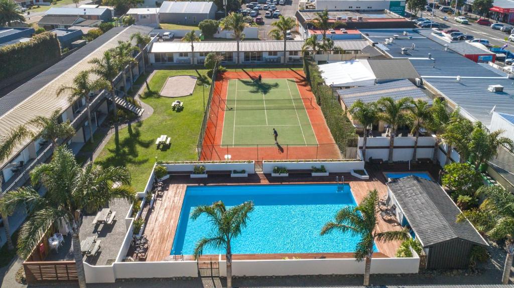 una vista aérea de una piscina con una pista de tenis y palmeras en Palm Pacific Resort & Motel en Whangamata