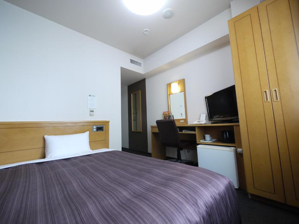 a hotel room with a bed and a desk and a television at Hotel Route-Inn Obihiro Ekimae in Obihiro