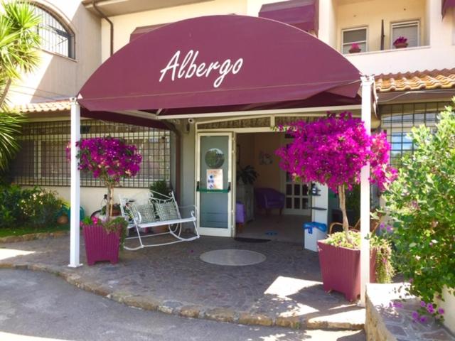 Hotel La Rosa Dei Venti في ألبينيا: متجر به مظلة أرجوانية أمام مبنى