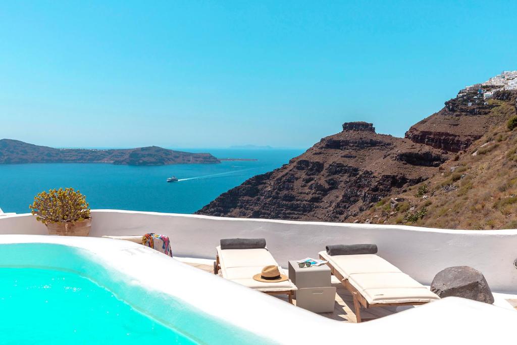 uma piscina com cadeiras e vista para o oceano em 180° Caldera by Stylish Stays em Firostefani