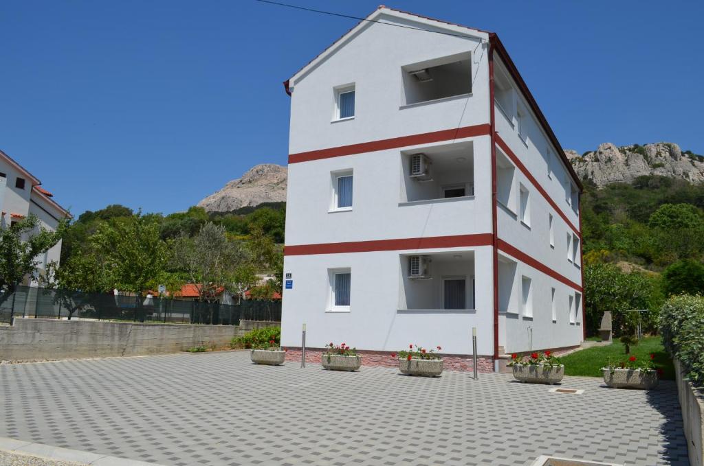 un bâtiment blanc et rouge avec des plantes en pot devant lui dans l'établissement Apartments Sušec, à Baška