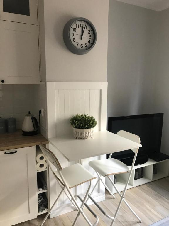 une table et des chaises blanches avec une horloge sur le mur dans l'établissement Apartament Wigilijna Starówka, à Elbląg