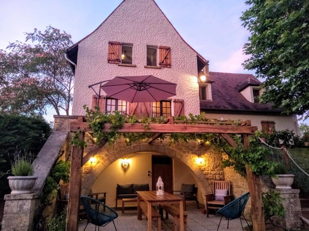 a house with an arbor with a table and an umbrella at AU SOLEIL COUCHANT in Saint-Julien-de-Lampon
