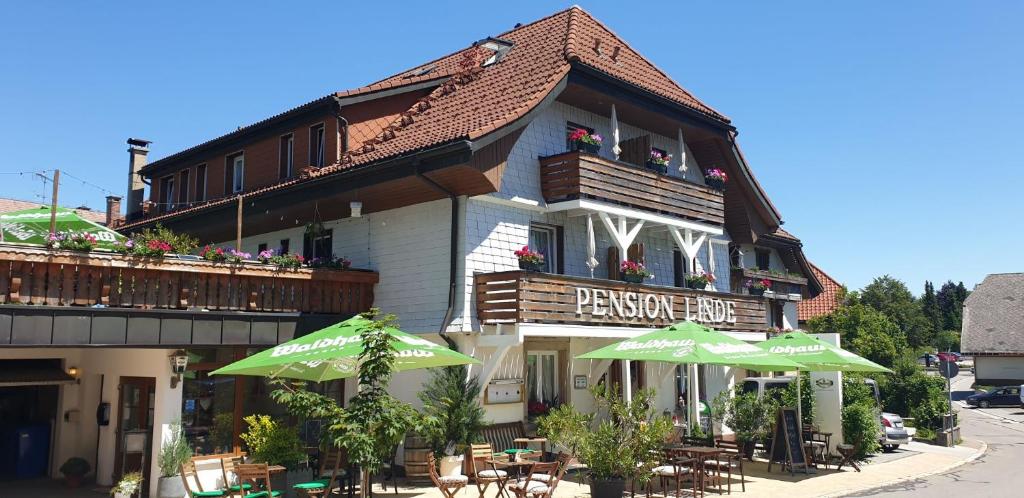 ein Gebäude mit Tischen und Sonnenschirmen davor in der Unterkunft Pension Linde in Höchenschwand