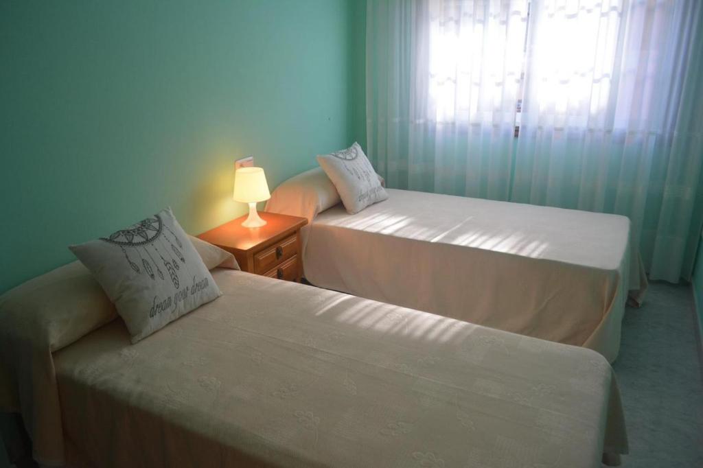 a room with two beds and a lamp and a window at Apartamentos baltar sanxenxo 1 in Sanxenxo