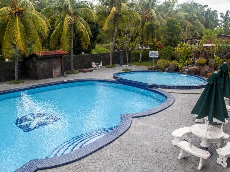 2 piscinas con sillas y sombrillas en un complejo en Hotel Seri Malaysia Bagan Lalang, en Sepang