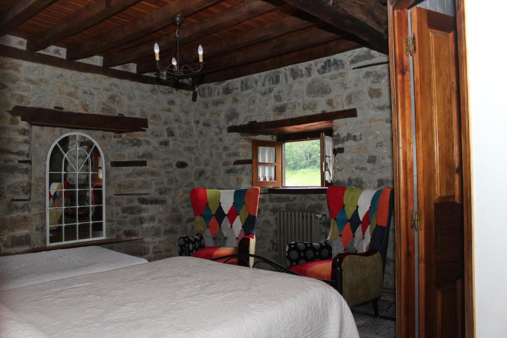 ein Schlafzimmer mit einem Bett und Stühlen in einer Steinmauer in der Unterkunft Casa Rural Sobrevilla II in Pido