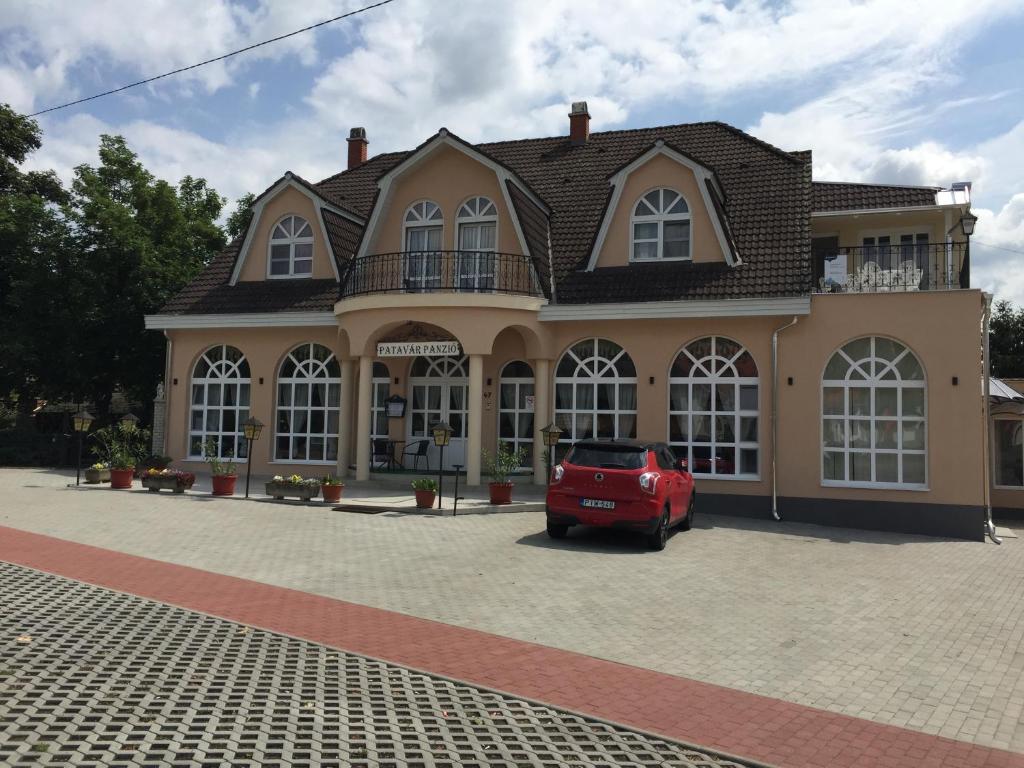 una casa con un coche rojo estacionado frente a ella en Patavár Panzió Étterem, en Gyöngyöspata