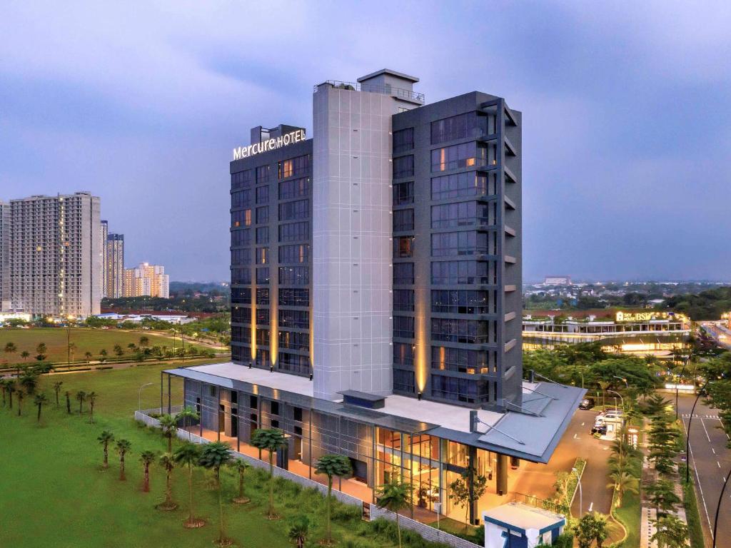 a tall white building with palm trees in front of a city at Mercure Tangerang BSD City in Tangerang