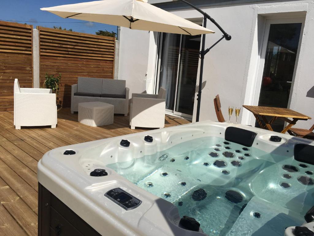 a hot tub sitting on a deck with an umbrella at Escale à 2 dans le Skiff, bord de mer et spa in Barneville-Carteret