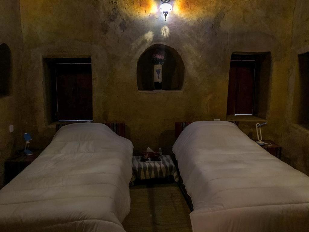 two beds in a room with two windows at Al Hamra Old House in Al Ḩamrāʼ