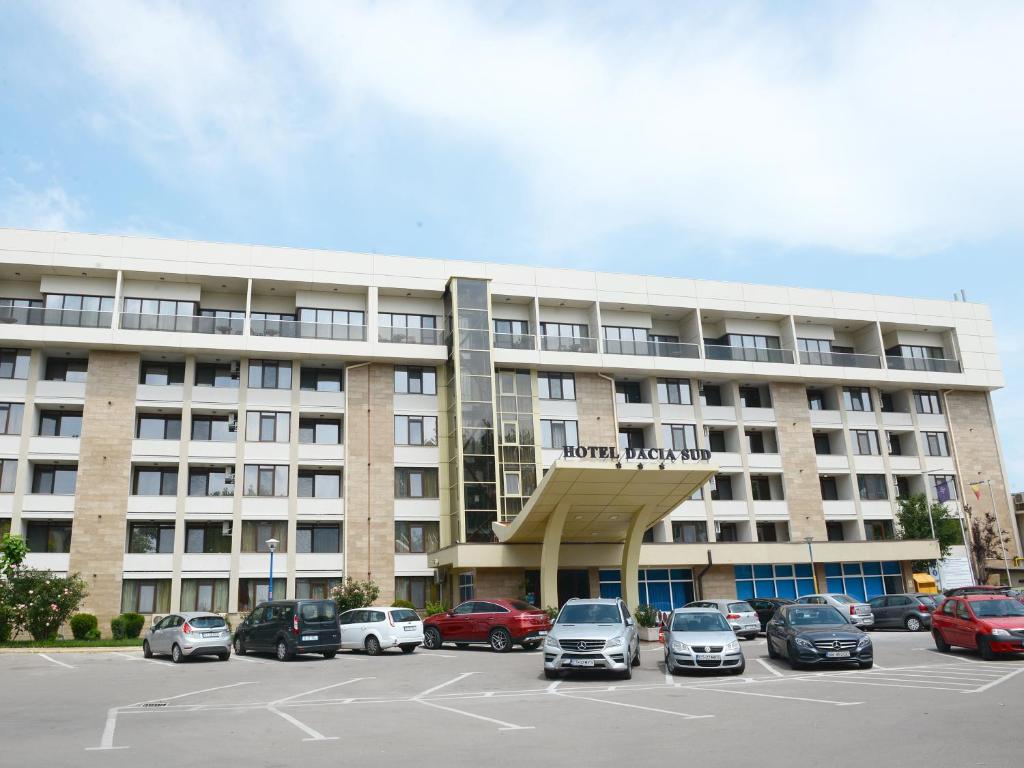 a large building with cars parked in a parking lot at Hotel Dacia Sud in Mamaia