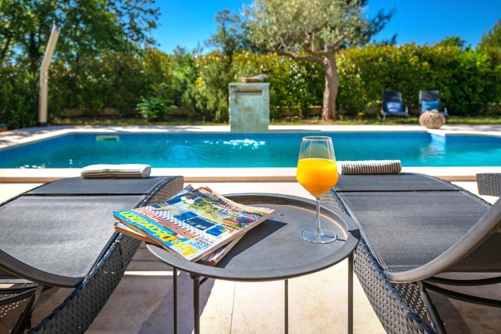 a table with a glass of orange juice next to a pool at Spacious holiday house - pool / jacuzzi / sauna / playground / 8+2 in Rakalj