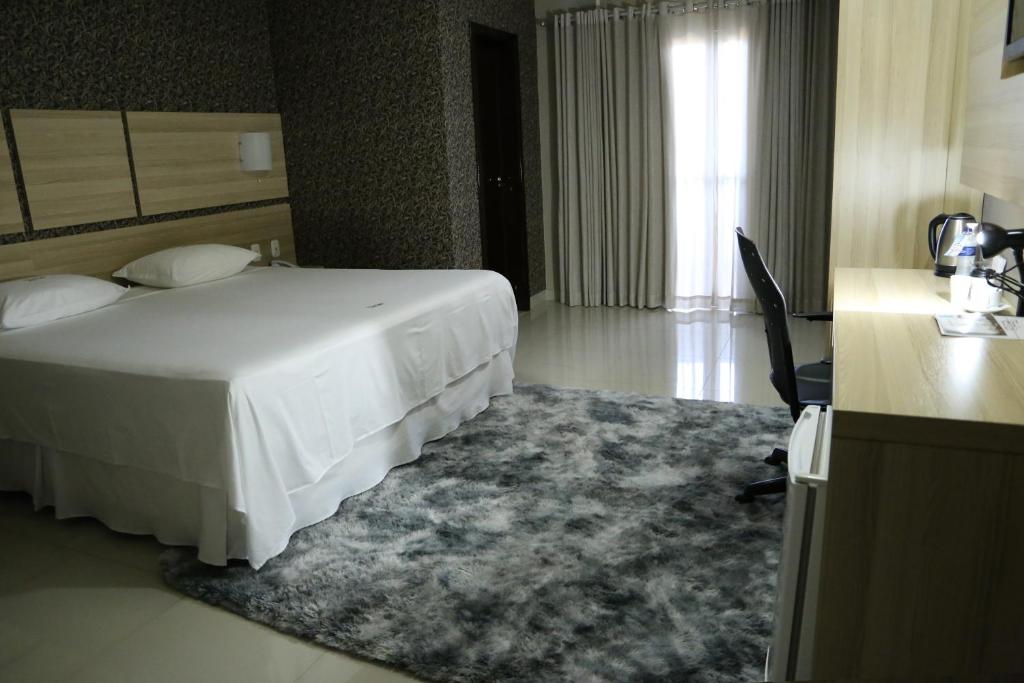 a hotel room with a white bed and a desk and a desk at Tezla Hotel in Primavera do Leste