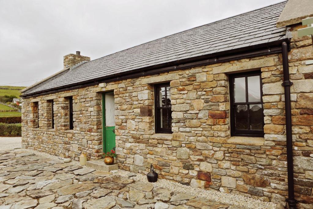 un edificio de piedra con una puerta verde y un gato sentado fuera en The Spinner's Cottage, en Donegal