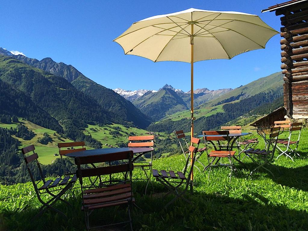 einen Tisch und Stühle mit einem Regenschirm auf einem Berg in der Unterkunft Hotel Alpina in Lumbrein