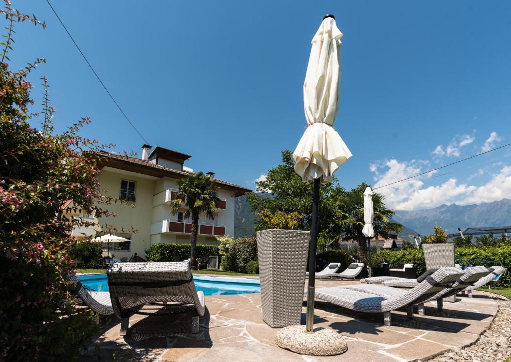- une terrasse avec des chaises et un parasol à côté de la piscine dans l'établissement Hotel Residence Martha, à Lana