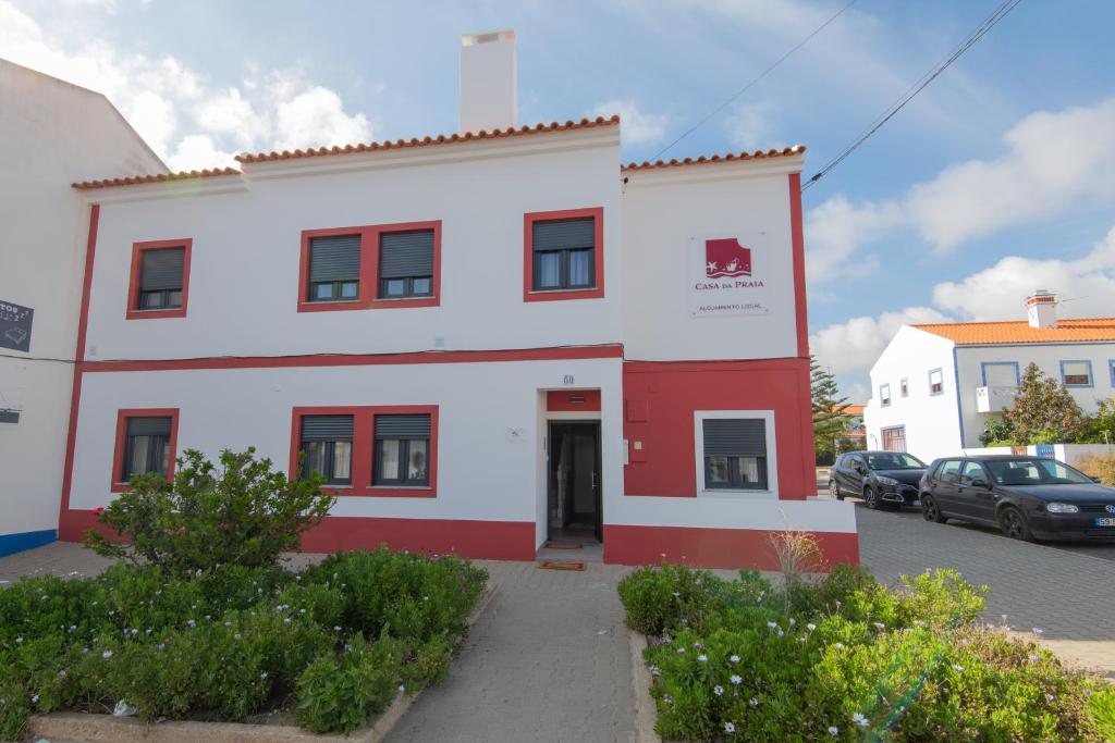 un bâtiment blanc et rouge avec des voitures garées dans un parking dans l'établissement Casa da Praia, à Zambujeira do Mar