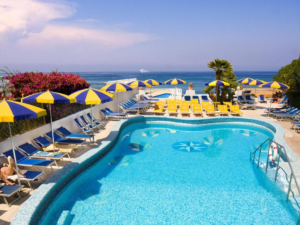 a swimming pool with chairs and umbrellas and the ocean at Hotel Ambasciatori in Ischia