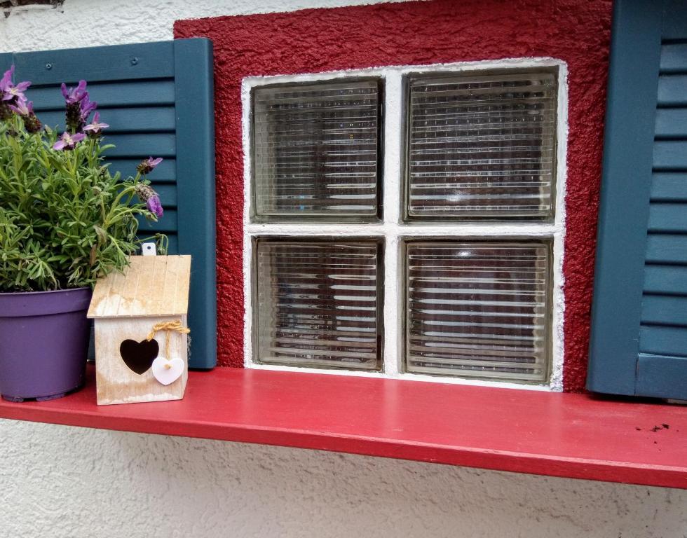 een raam met een pot bloemen op een rode vensterbank bij Mein Häuschen in Maikammer