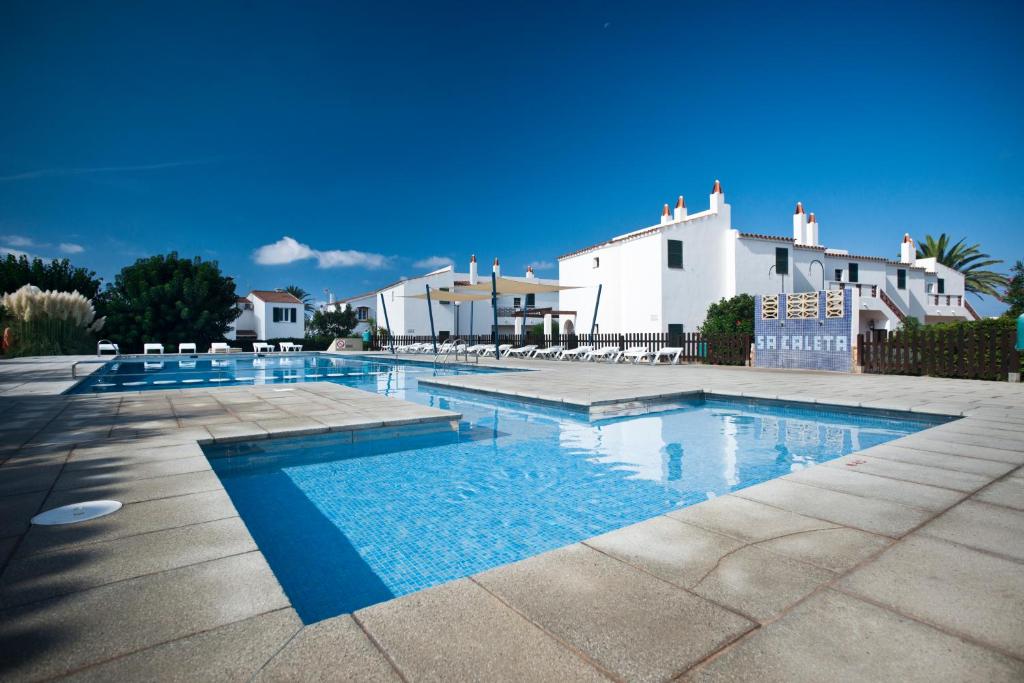 a swimming pool in front of a white house at Apartamentos Sa Caleta in Sa Caleta