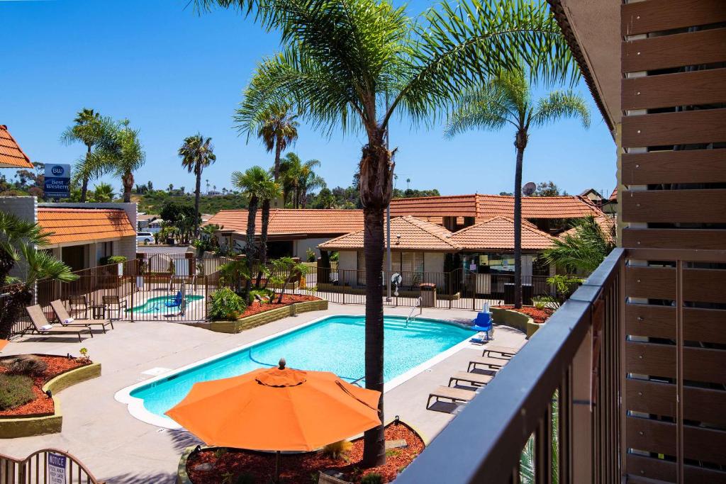 an orange umbrella next to a swimming pool with palm trees at Best Western Oceanside Inn in Oceanside