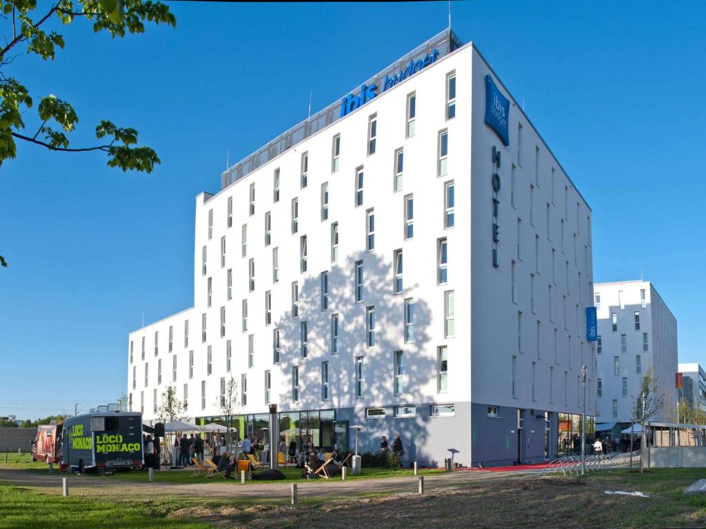 un edificio blanco alto con gente delante de él en ibis budget Muenchen City Olympiapark, en Múnich