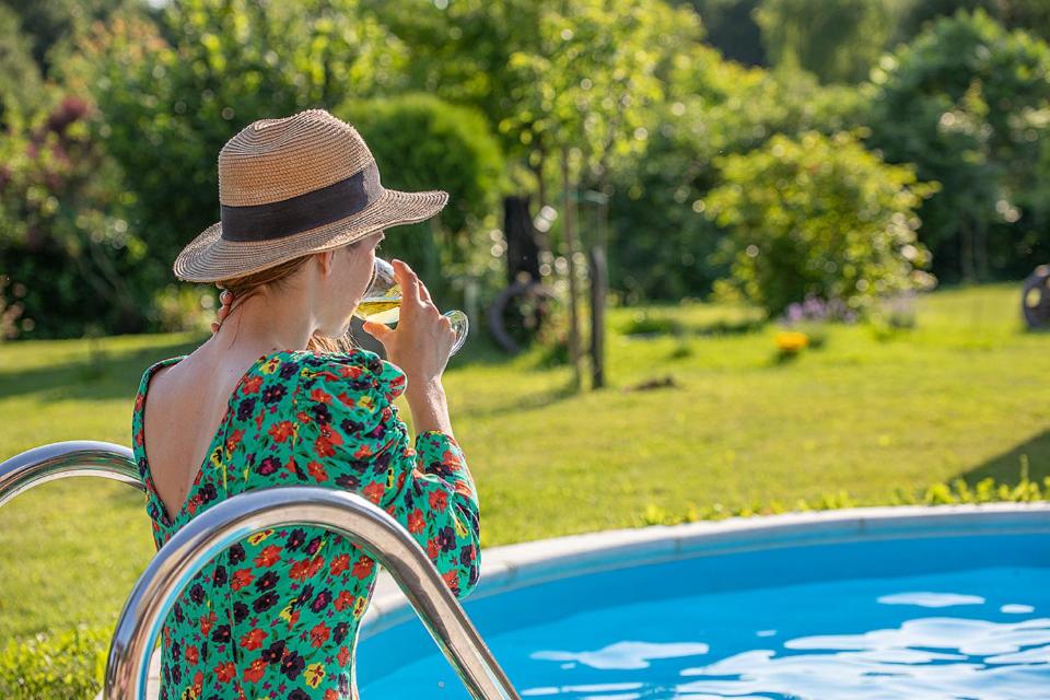 a woman in a hat talking on a cell phone next to a pool at Holiday Home Arcadia with pool, hot tub and sauna in Pleškovec