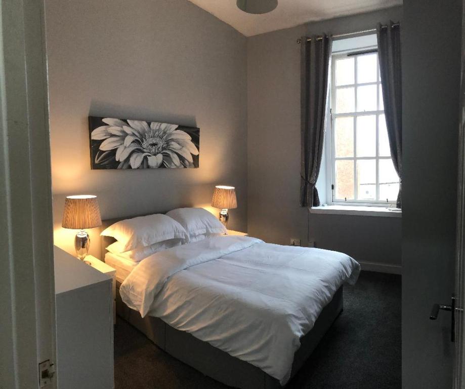 a bedroom with a bed with two lamps and a window at The Station Apartment in Kilmarnock