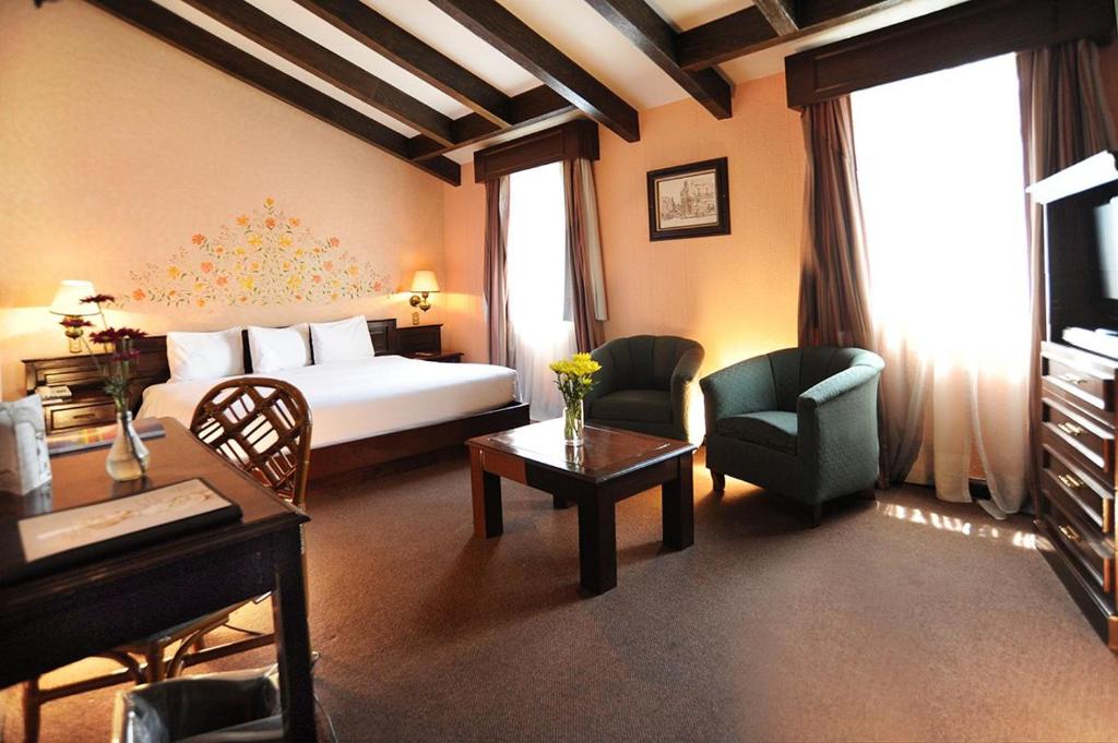A bedroom with a large bed also includes two armchairs, a coffee table, and a compact desk.