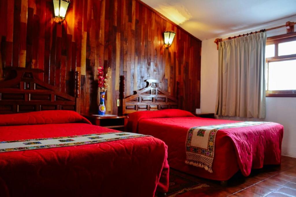 a bedroom with two red beds and a window at Meson Yohualichan in Cuetzalán del Progreso
