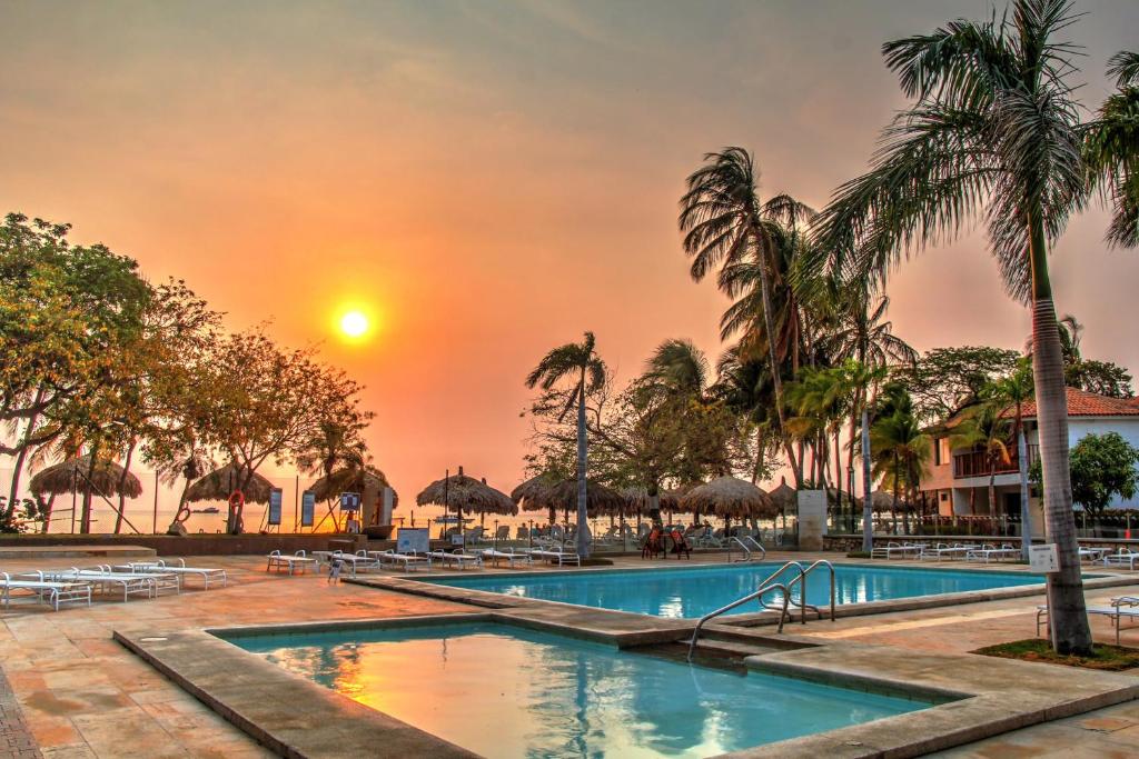 a pool at a resort with a sunset in the background at Estelar Santamar Hotel & Centro De Convenciones in Santa Marta