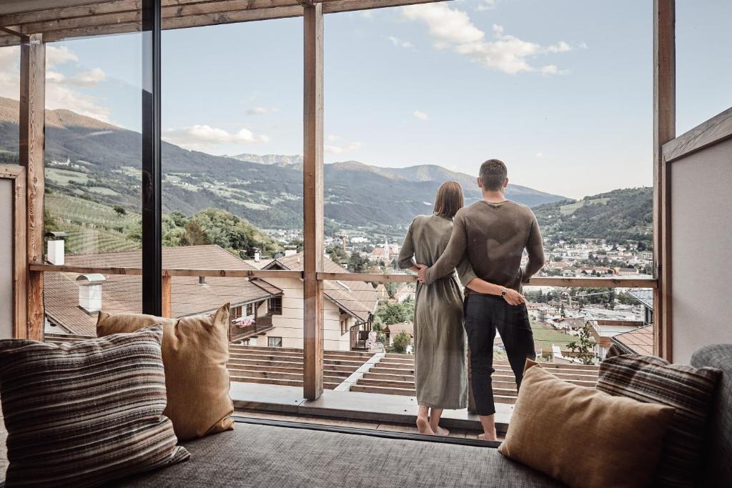 Una pareja de pie en un balcón con vistas a las montañas en Haller Suites & Restaurant, en Bresanona