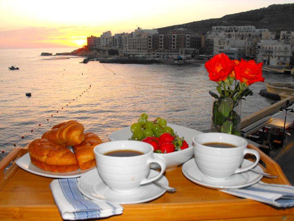 a table with two cups of coffee and croissants and flowers at Marsalforn Sea View Beachfront Studio Apartment in Marsalforn