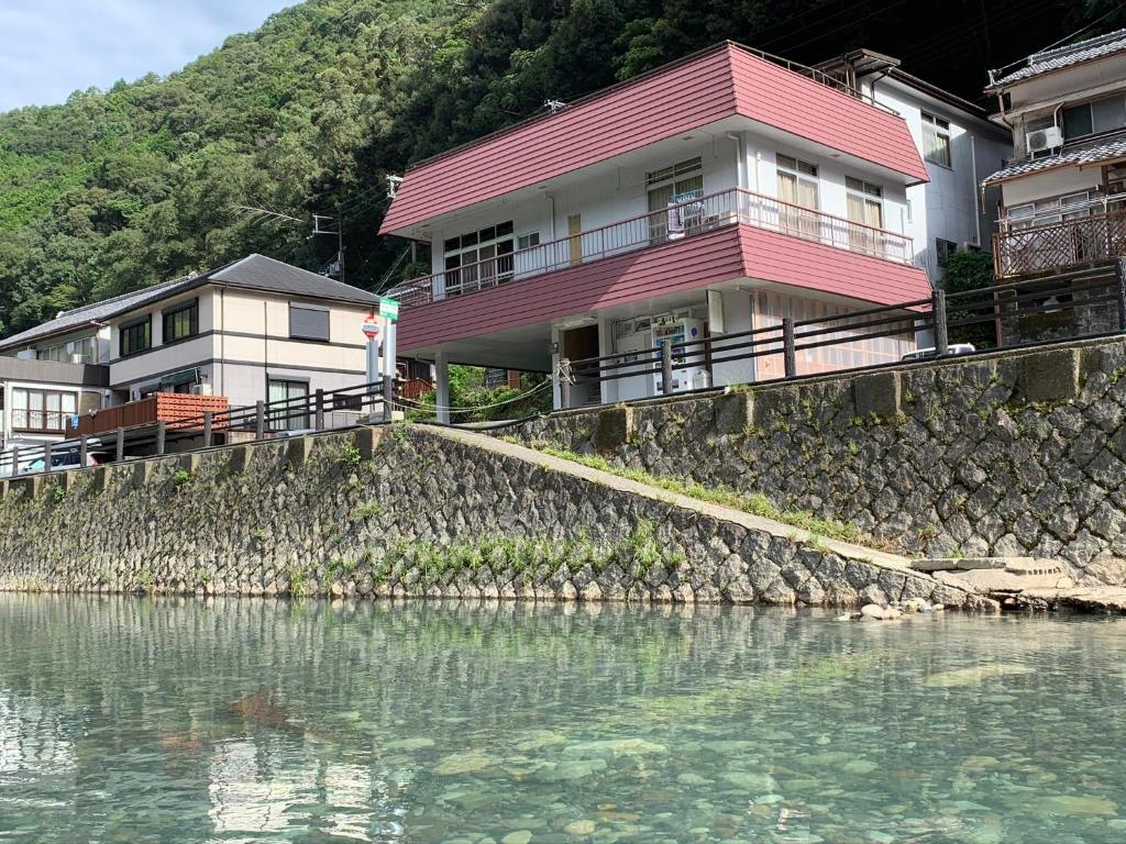 a house on top of a rock wall next to the water at Minshuku Sumiya in Tanabe