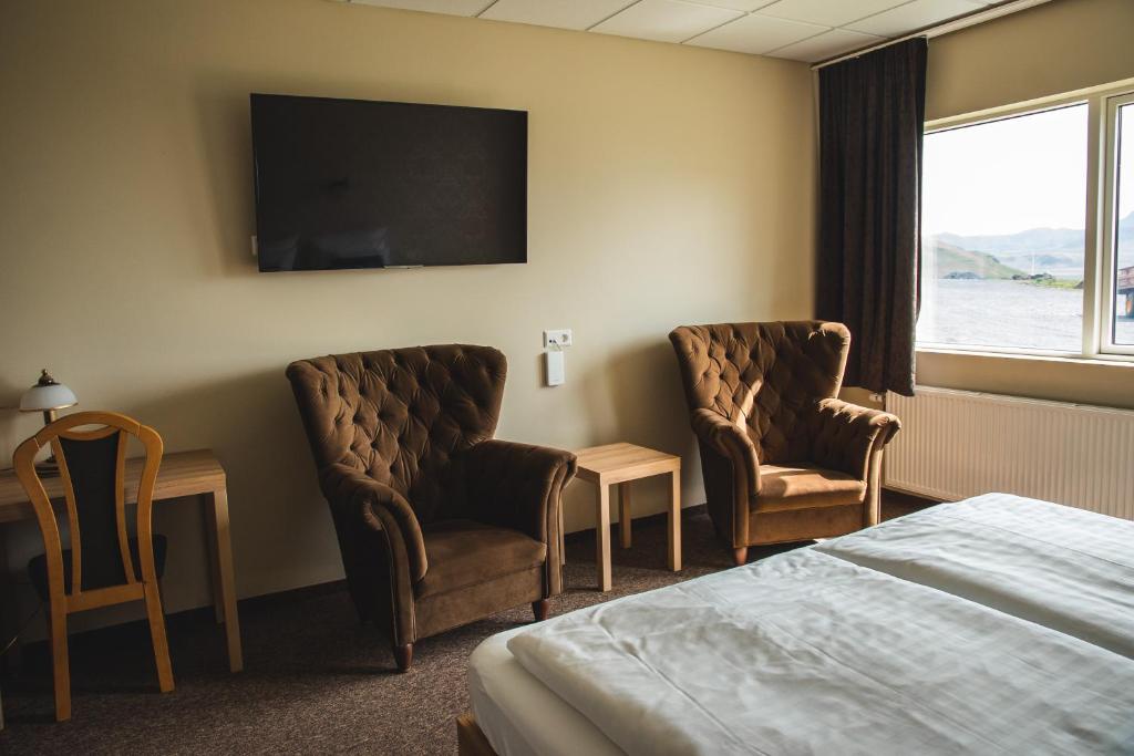 a hotel room with two chairs and a bed and a television at Hótel Dyrhólaey in Vík