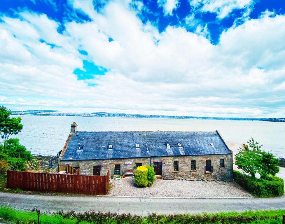 uma casa antiga com painéis solares na água em The Old Boathouse em Wormit