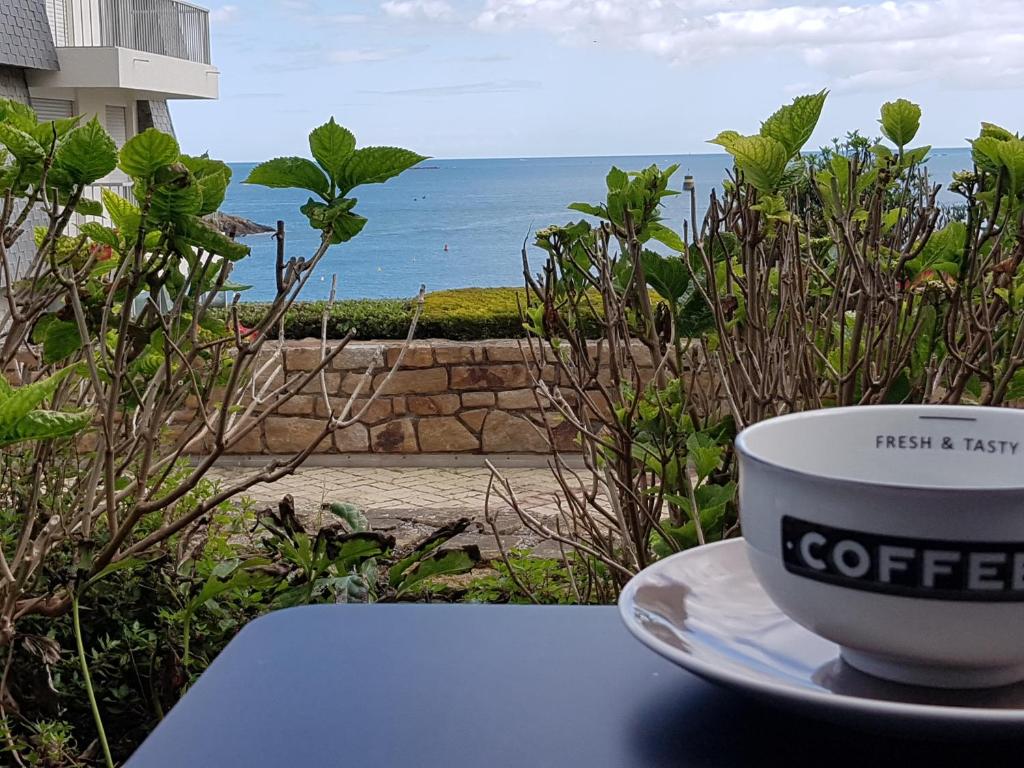 - une tasse de café assise sur une table à côté de l'océan dans l'établissement Les pieds dans l'eau, à Saint-Quay-Portrieux