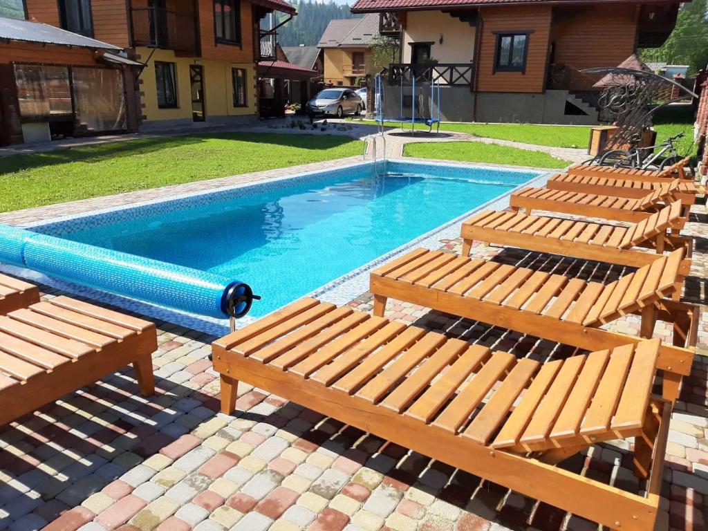 a pool with three wooden benches and a swimming pool at Садиба у Кіри in Slavske