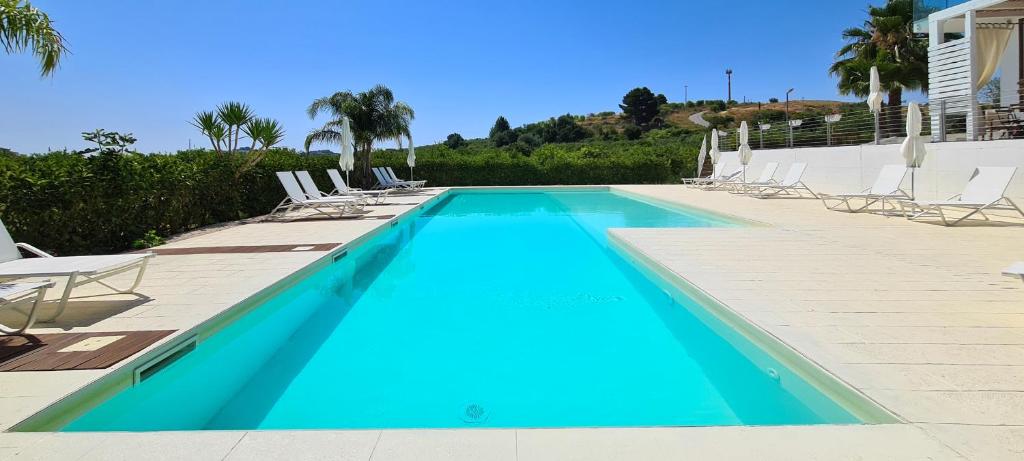 a blue swimming pool with chairs and palm trees at Villa Landolina in Noto