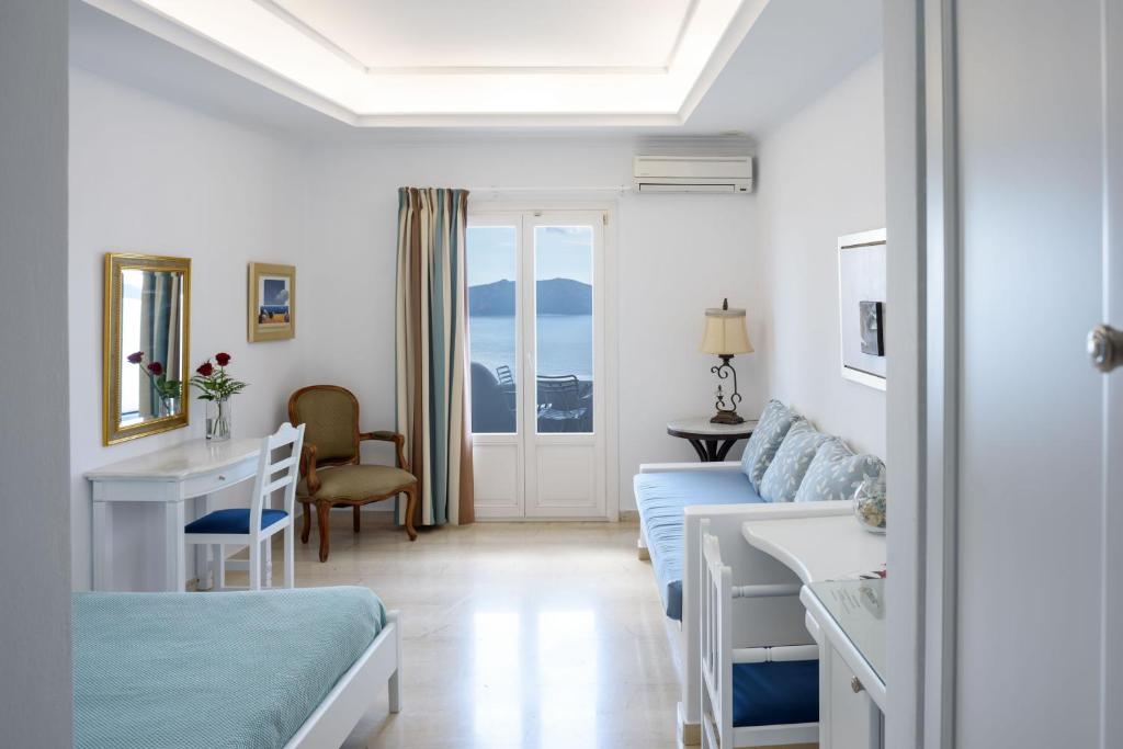a white room with a bed and a desk and a couch at Villa Renos Hotel in Fira