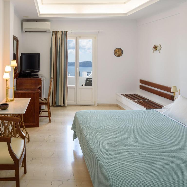 a bedroom with a bed and a table and a window at Villa Renos Hotel in Fira