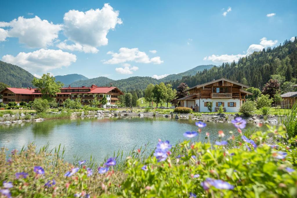 a pond in a village with mountains in the background at Relais & Châteaux Gut Steinbach Hotel Chalets SPA in Reit im Winkl